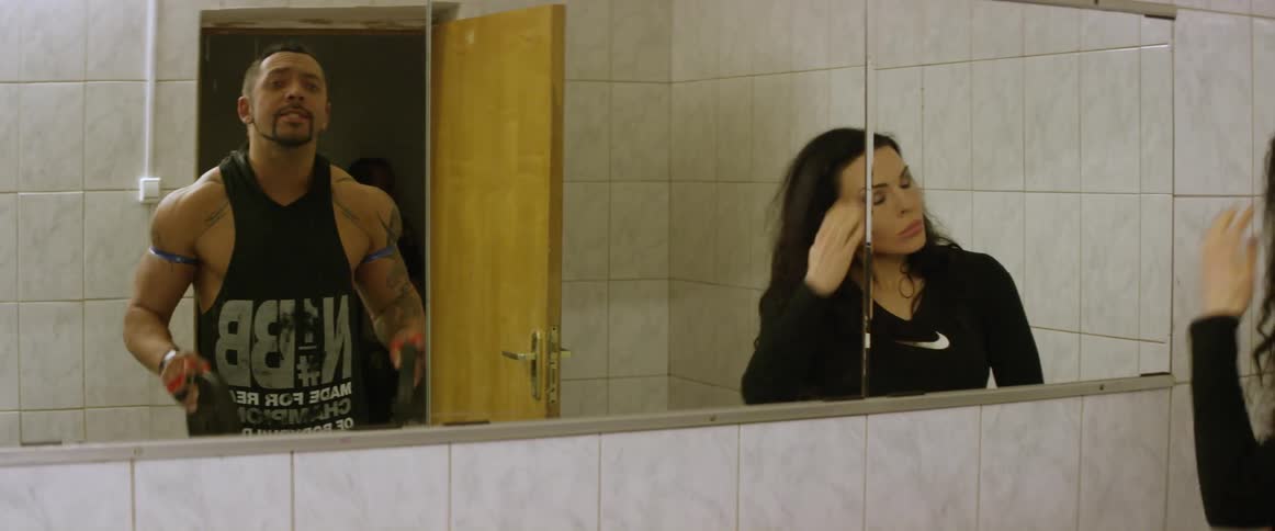 Man lifts weights and woman fixes hair while looking in a mirror
