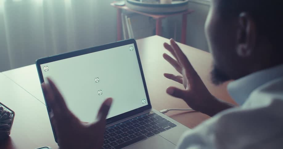 A man sits at a desk using a laptop with a blank screen showing placeholder icons