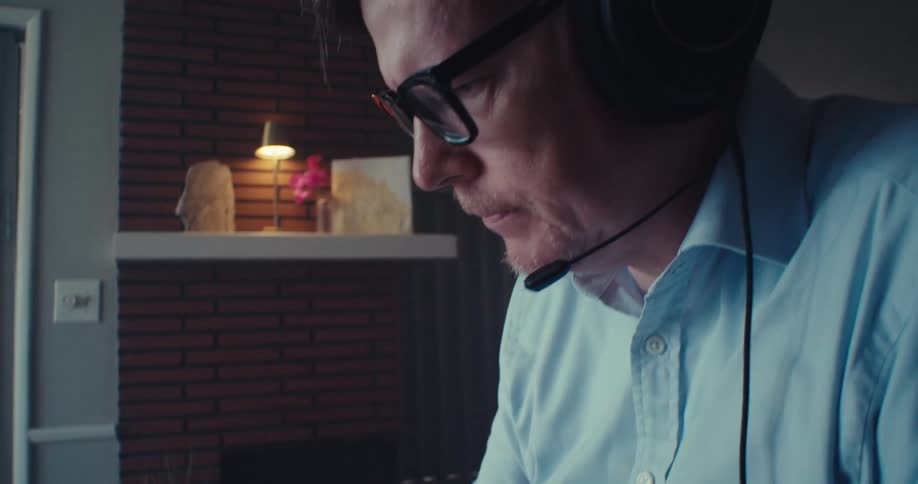 A man wearing headphones works on a laptop in a home office