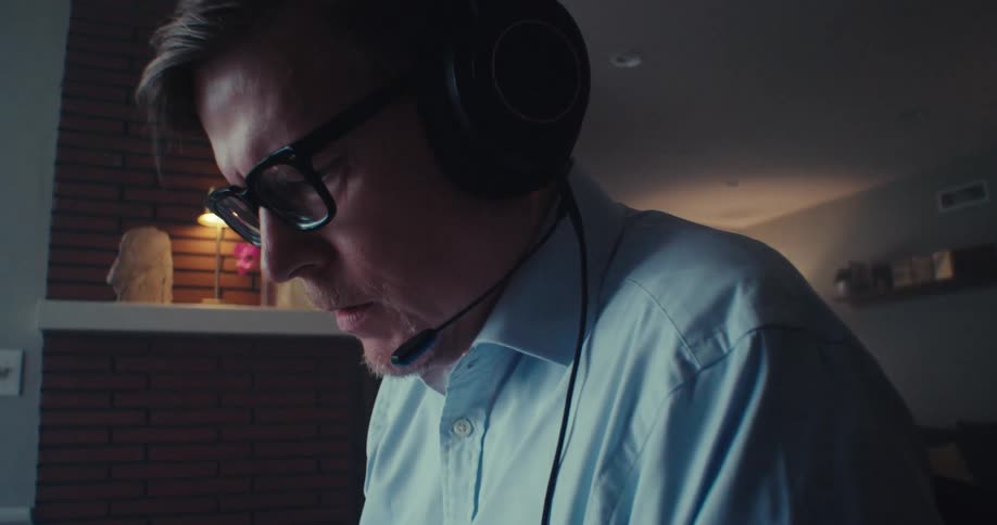 Man with headphones works intently at desk in dim home office