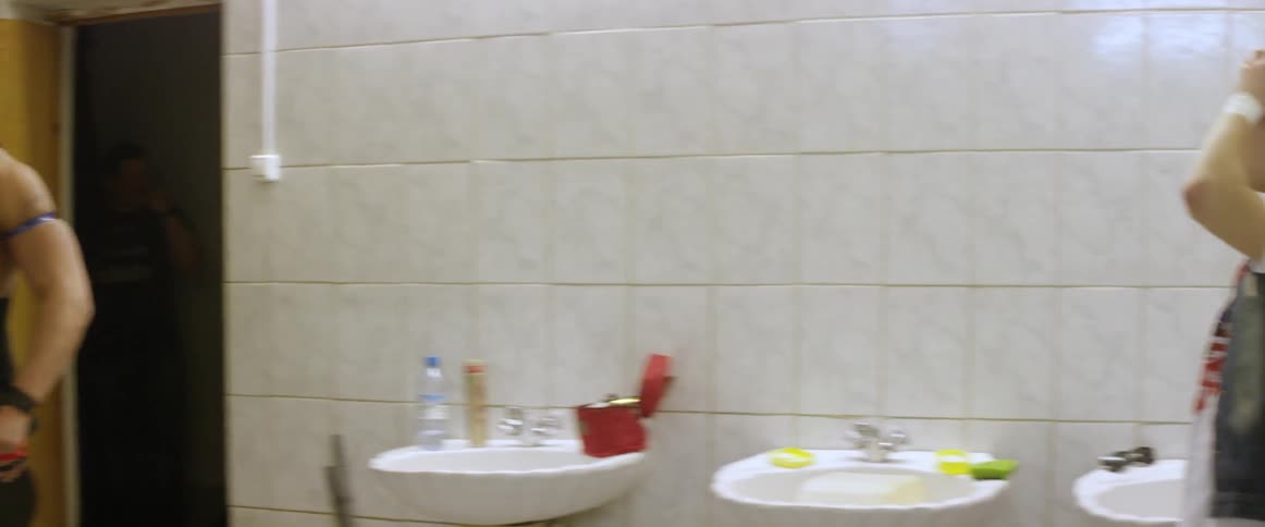 A man lifts weights in a bathroom while another watches