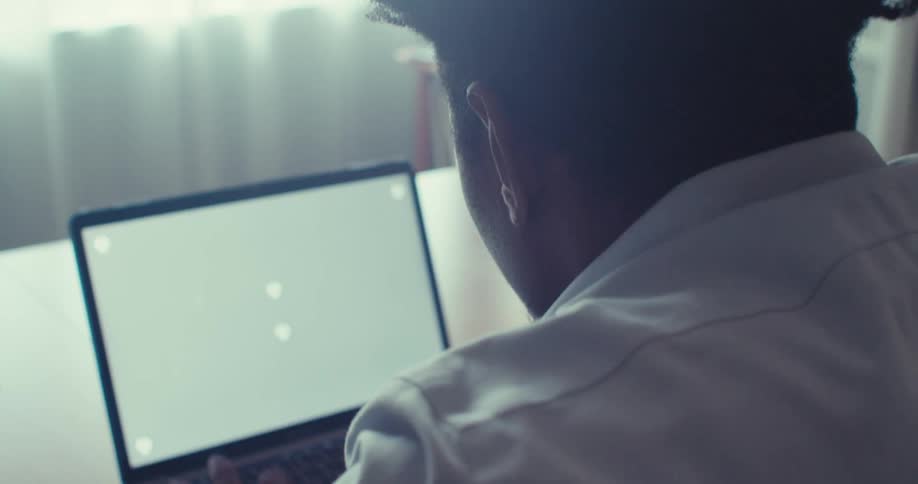 A man works intently on a laptop at a desk seen from behind