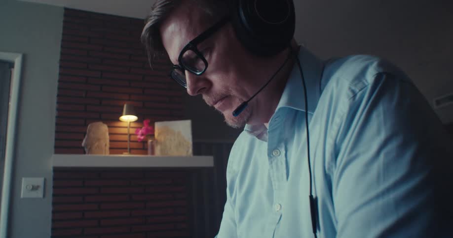 A man wearing headphones is typing on a laptop on the table in front of him