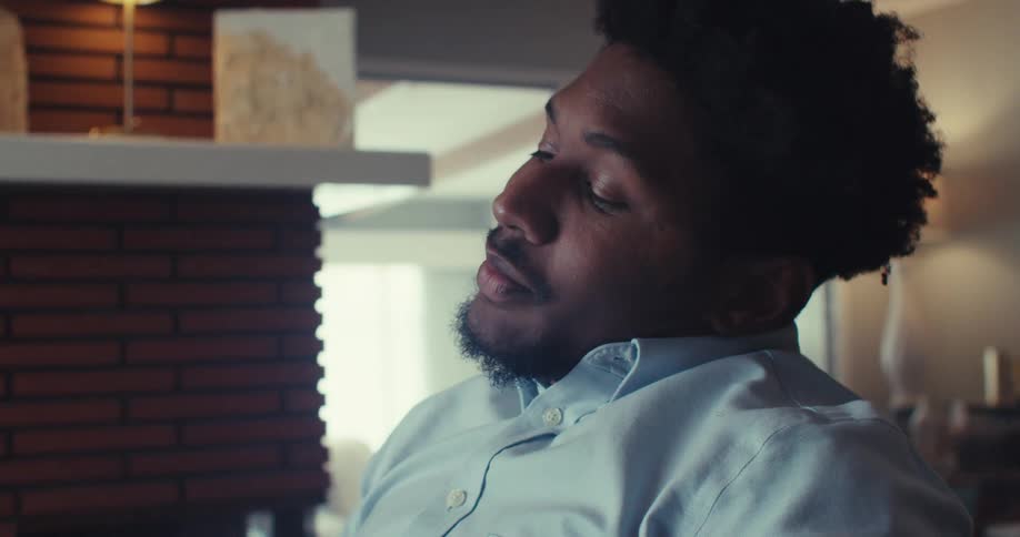 A young man working from a home office sits behind a desk looking disappointed