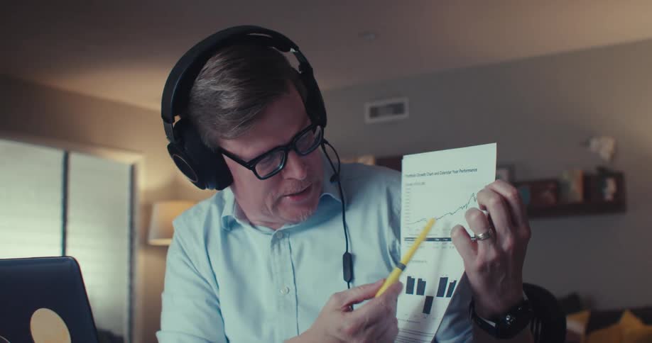 A man wearing headphones is holding a pen pointing to a paper with a graph