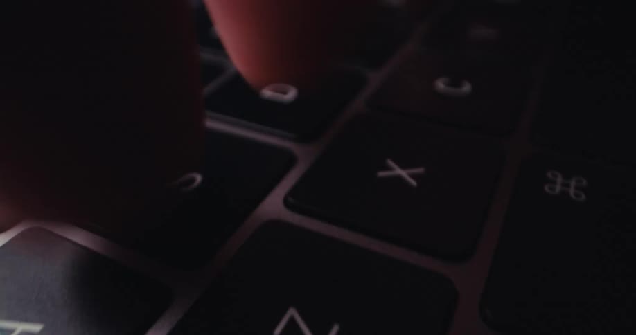 Fingers tap flat black keys with white lettering on the keyboard of a gray laptop