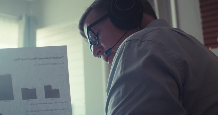 Man on a call studies a printed stock chart in a brightly lit office
