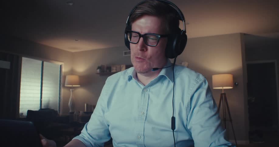 A man in headphones smiles and gestures while video conferencing at home
