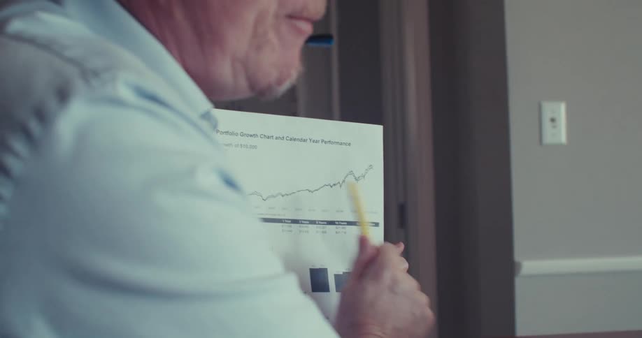The face of a man wearing headphones and using a yellow pen to point to a graph paper while looking at a laptop screen