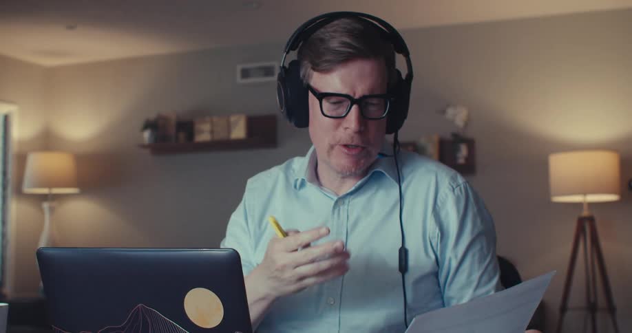 A man wearing a headset points to a printed chart during a video call in a home office setting