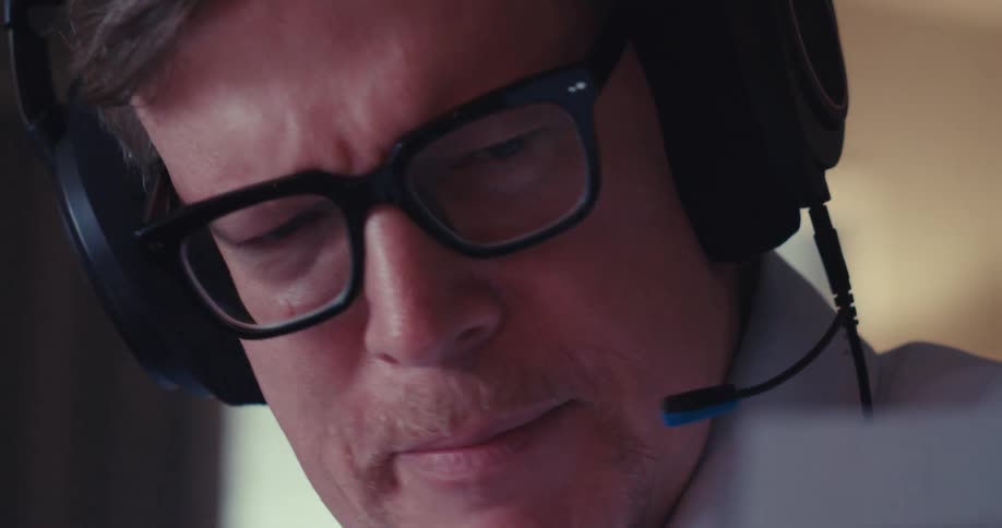 A man wearing headphones sits at a desk explaining and reviewing documents