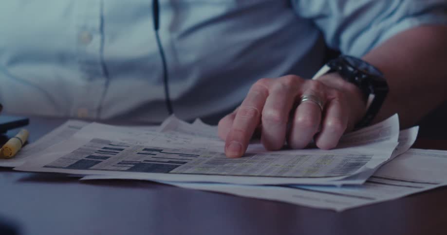 A man working from home wearing headphones reading documents at a desk with a laptop