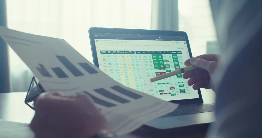 A person reviews graphs on their paper and information on their computer