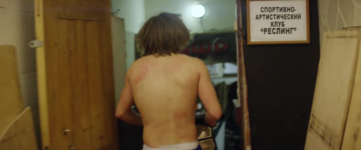 A wrestler with bruises on his body moves down a stairway and hall
