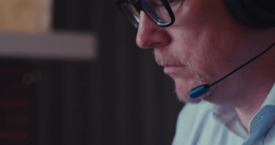 Closeup of a man typing on a laptop while wearing a headset