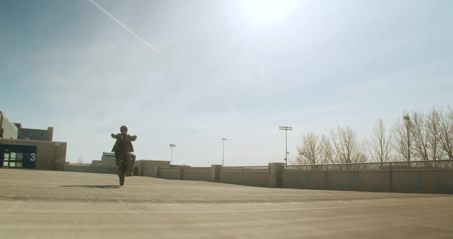 Man does wheelie on electric moped in a parking lot under bright sun