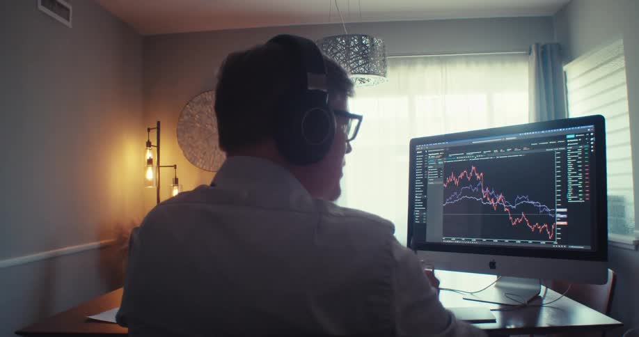 Man in headphones points at stock charts on a computer screen during a video call