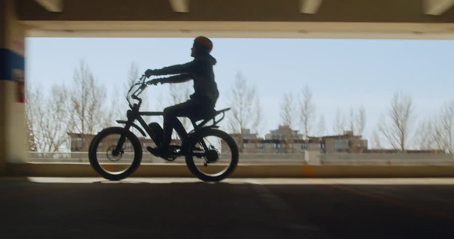Man cruises through parkade on his bike silhouetted by blue sky.