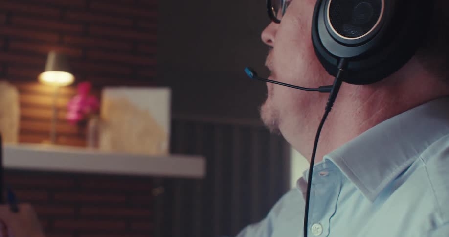 A person wearing headphones closely examines a computer screen displaying two fluctuating line graphs tracking financial or data trends