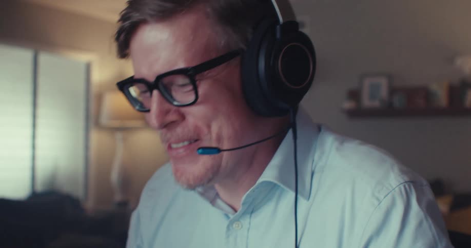 Man speaking on a headset during a video call on his computer smiles while working from his home