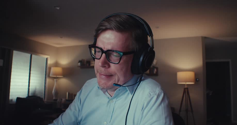 A man wearing a headset intently analyzes stock charts on his computer while speaking