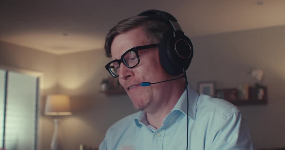 The face of a man who is wearing headphones and he is talking to someone through his laptop and he is happy