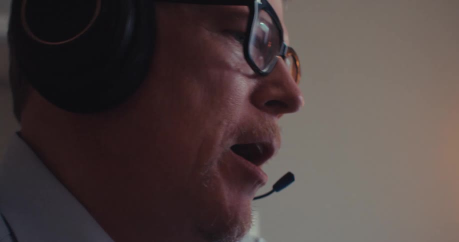 The man is talking with someone on his headset and looking at information on his computer
