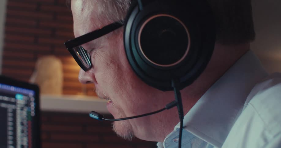The man is talking with a headset by his monitor