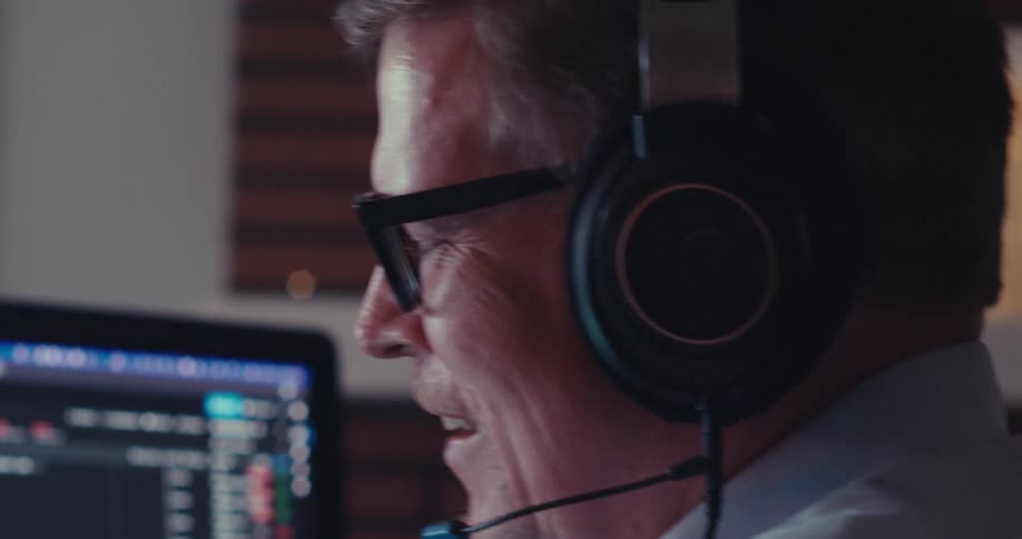 A person wearing headphones sits at a desk analyzing stock market graphs on a computer screen