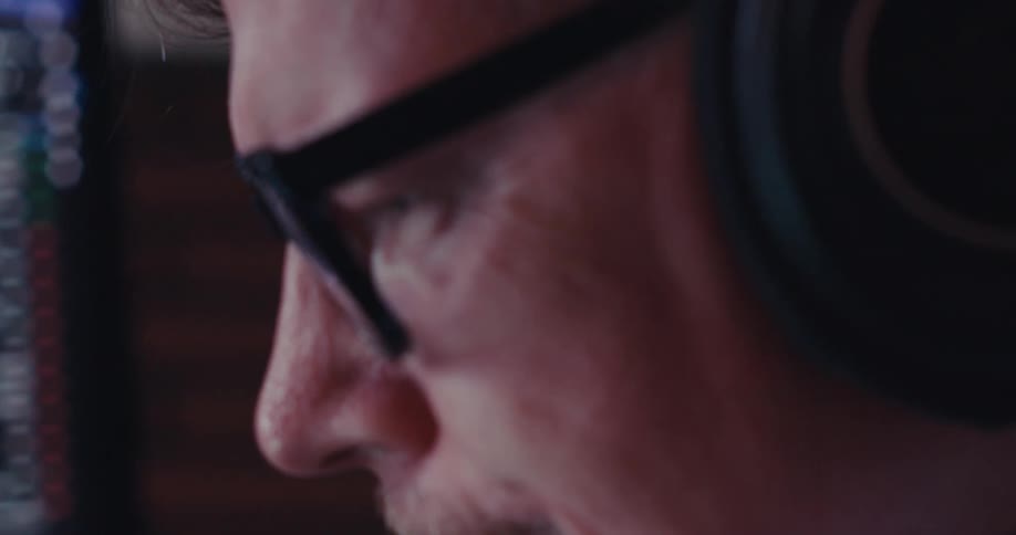 A man wearing headphones intensely monitors falling stock charts on his computer screen