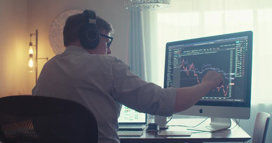 A trader wearing headphones looks at a stock market price chart on a computer monitor