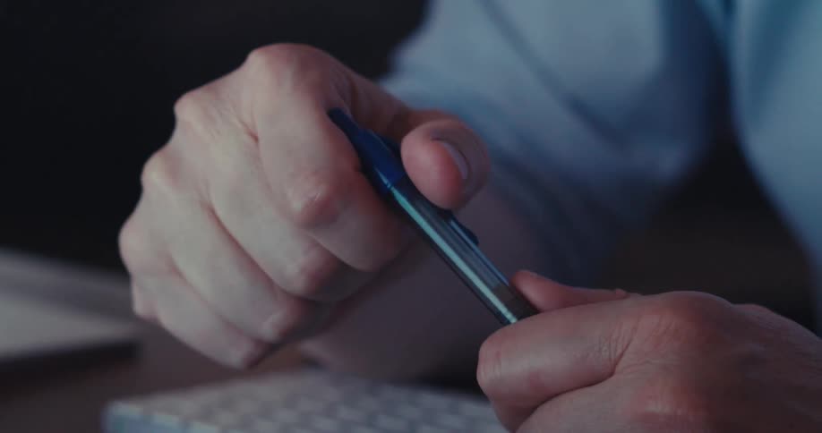 A closeup of a man wearing glasses and headphones staring thoughtfully at a pen in his hands