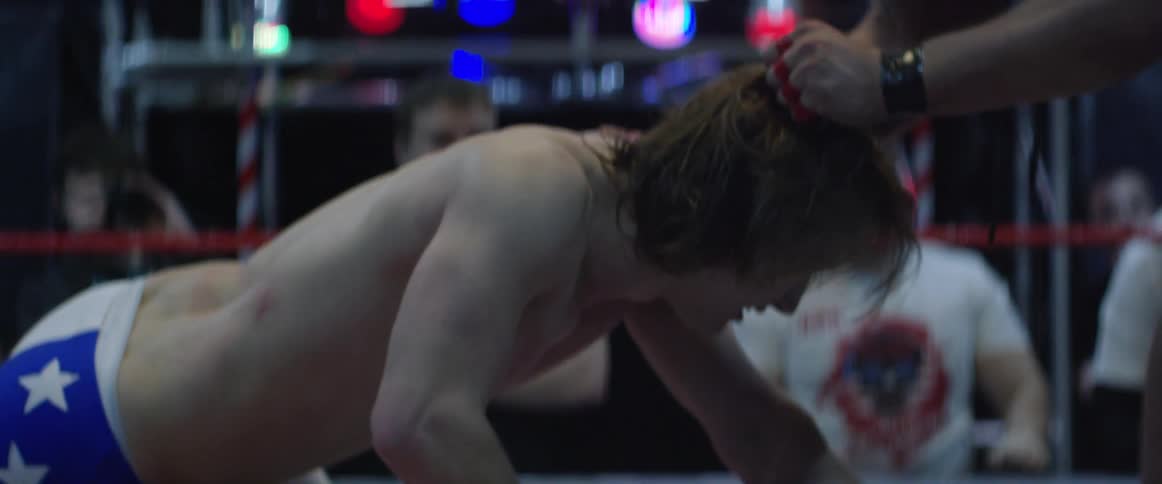 A wrestler is lifted from the ground by his hair in a wrestling ring