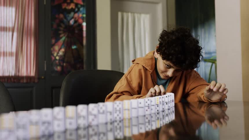 A little boy is knocking over a row of dominoes that are stacked on a table