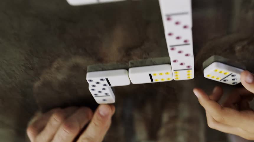 Upside down perspective of people placing dominoes on a stone surface