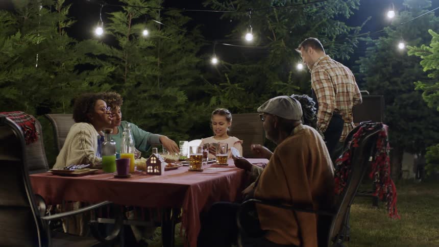 Family enjoy an outdoor dinner under string lights at night
