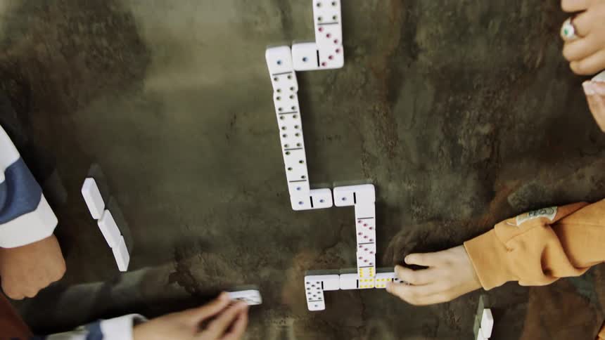 The hands of some people placing pieces in a domino game on a smooth table