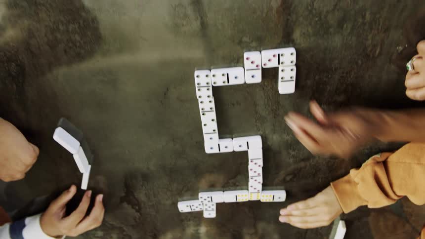 Hands of people placing white dominoes on a smooth marble surface