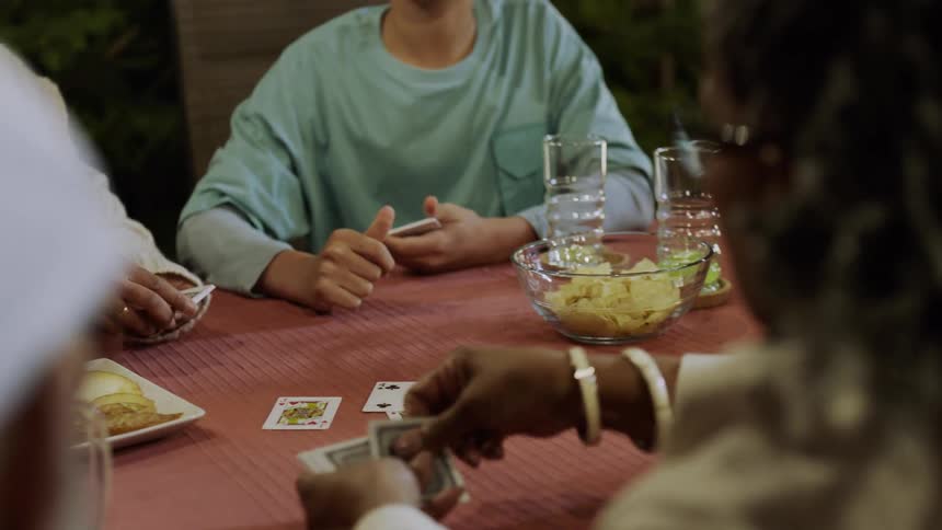 A group of people joyfully play cards together at a table outdoors