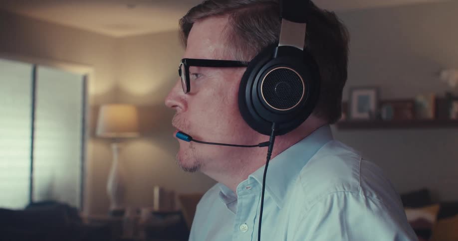 A person wearing headphones is on a call near a computer screen showing two fluctuating line graphs tracking data or financial trends