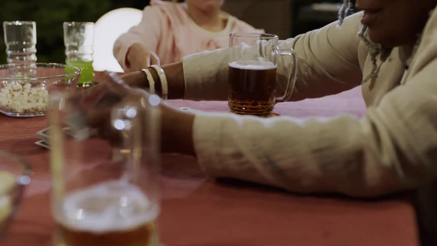 A family sits around a table playing cards with a bowl of popcorn and drinks nearby