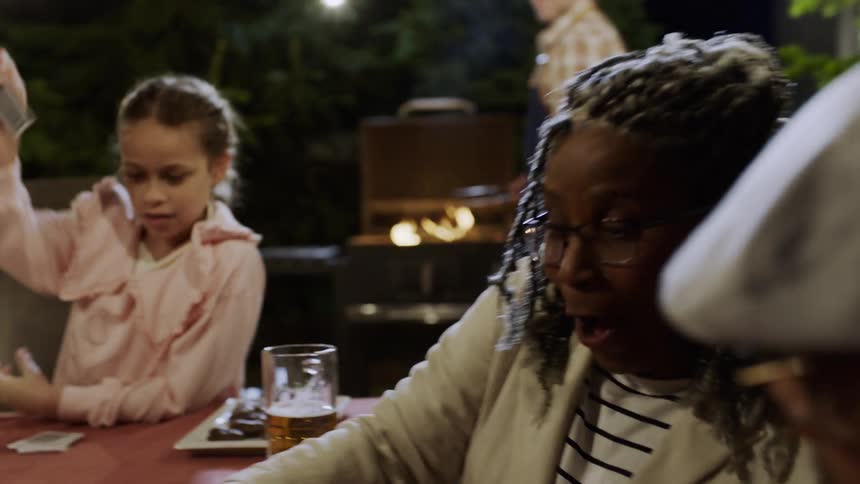A family enjoys an evening together grilling and playing cards outside on their patio