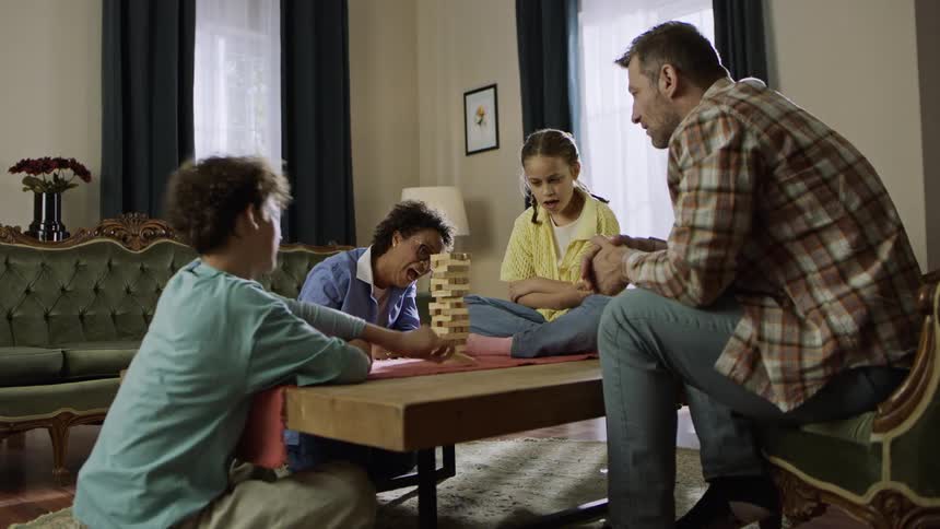 Family gather around a coffee table playing a block stacking game in a cozy living room