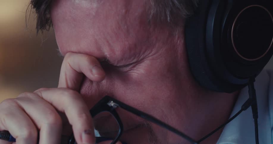 A man wearing headphones and eyeglasses looks disappointed