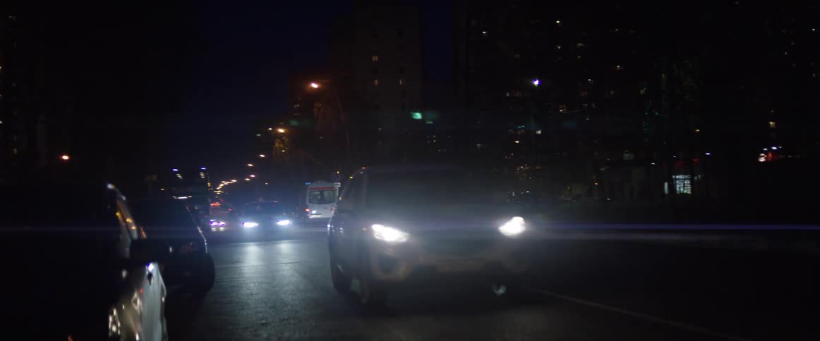 An ambulance with blue lights drives a city street at night