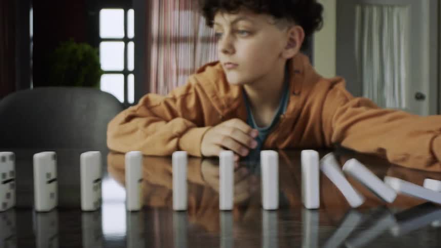 A teenage boy placing dominoes one after the other and then knocking one of them down and creating a cascading effect