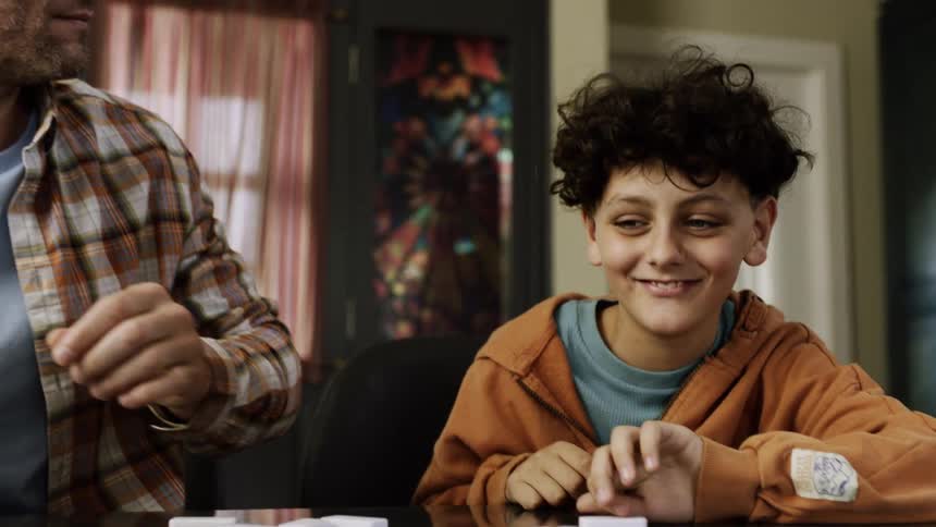 A father and son sit at a table playing dominoes together sharing a fun and focused moment