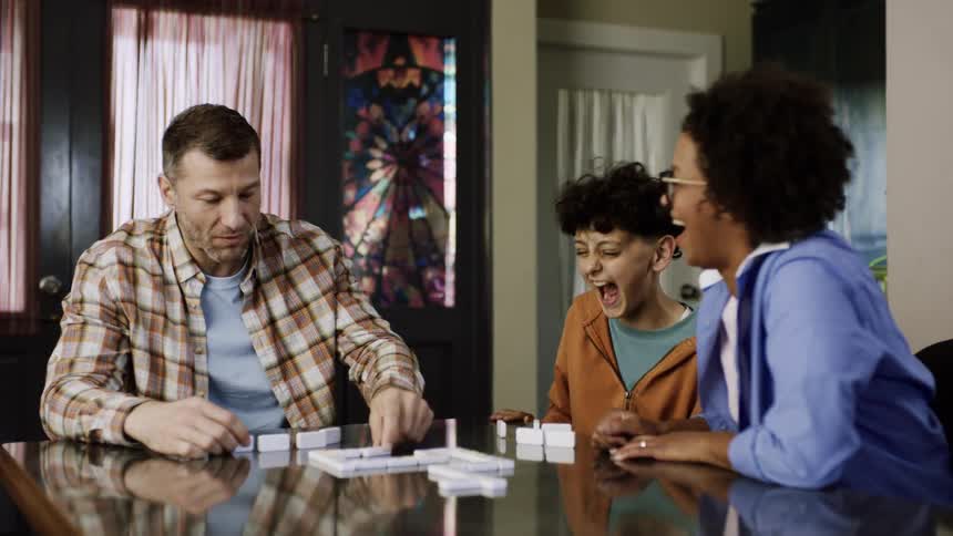 A woman laughs as she plays dominoes with her family