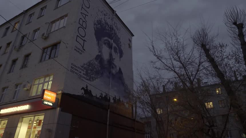 A mural of a russian man adorns the side of a multistory building