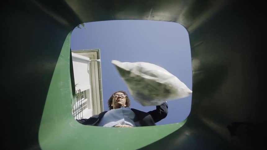 A woman throws trash into a bin seen from inside the bin looking up